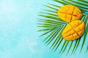 A-Tantalisingly-Tropical-Mango-Ice-Cream-image-3-jpeg-Mango-cut-into-cubes-on-palm-tree-leaves-with-tropical-sea-blue-background-frosted-fusions.