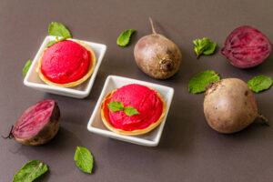 Homemade-Beetroot-Ice-Cream-Naturally-Sweet-Vibrant-image-6-scoops-of-fresh-beetroot-ice-cream-in-white-dishes-with-raw-beetroot-and-fresh-geeen-leaves-scattered-frosted-fusions