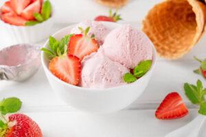 Scrumptious-Strawberry-ree-Ice-Cream-A-Burst-of-Juicy-Goodness-image-3-white-bowl-with-scoops-of-strawberry-ice-cream-waffle-cone-and-fresh-strawberries-in-background-frosted-fusions