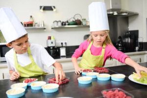 Berrylicious-Homemade-Raspberry-Sorbet-image-5-jpeg-2-kids-in-chefs-hats-involved-with-cooking-with-raspberries-in-kitchen-with-equipment-around-them-frosted-fusions