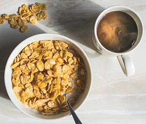 a-homemade-crunchy-cornflake-ice-cream-recipe-image-1-top-view-bowl-of-cornflakes-with-cup-of-coffee-to-the-side-and-some-scattered-cornflakes-rotated-frosted-fusions