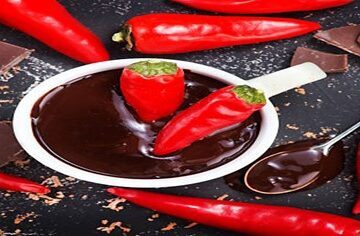 Homemade-Chilli-Chocolate-Ice-Cream-Sweet-and-Spice-Fusion-featured-image-200x600w several red chillis scattered with chunks and shavings of chocolste plus 2 red chillis in white bowl of chocolate sauce frosted fusions