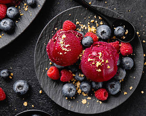 A Refreshing and Healthful Homemade Blueberry Sorbet image 3 blueberry sorbet on black plate with blueberries and raspberries scattered dark background frosted fusions
