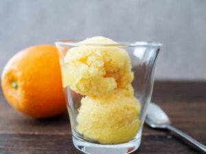 Whip-up-a-Boozy-Homemade-Vodka-and-Orange-Sorbet-image-2-glass-filled-with-orange-sorbet-with-an-orange-in-background-and-a-silver-spoon-frosted-fusions