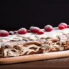 Christmas-Ice-Cream-Desserts-to-Sweeten-Your-Festivities-featured-image-200x600w-yule-log-decorated-with-berries-and-icing-sugar-and-festive-decorations-in-the-background-frosted-fusions
