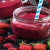 A-Delicious-And-Nutrient-Packed-Berry-Blast-Smoothie-featured-image-200x600w-reddish-pink-smoothies-glass-jars-several-types-of-berries-scattered-fresh-green-leaves-frosted-fusions