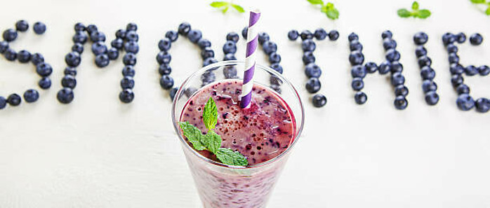A Delicious And Nutrient-Packed Berry Blast Smoothie image 2 glass of berry smoothie with green leaves to top and smoothie spelled with blueberries in background frosted fusions
