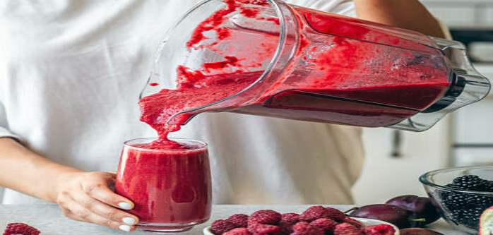 A Delicious And Nutrient-Packed Berry Blast Smoothie image 9 red berry smoothie mix being poured from a blender jug into a glass with selection of berries scattered frosted fusions