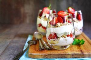 Strawberries-And-Cream-Homemade-Parfait-Ice-Cream-image-1-three-glasses-of-strawberries-and-cream-parfait-beautifully-layered-on-wooden-board-with-spoons-frosted-fusions