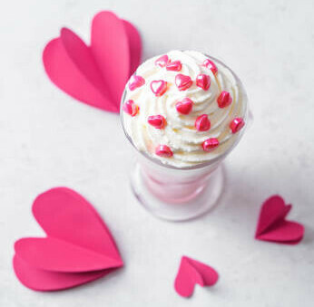 Homemade Ice Cream Treats For Valentines Day image 2 ice cream in glass dish with pink paper hearts scattered and pink heart sprinkles frosted fusions
