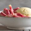 Homemade-Rhubarb-And-Custard-Ice-Cream-Recipe-featured-image-632x1950-bowl-of-rhubarb-and-custard-ice-cream-with-fresh-rhubarb-and-glass-of-custard-in-background-frosted-fusions