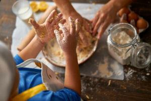 easy-homemade-cookie-dough-ice-cream-recipe-image-1-childs-hands-covered-in-dough-whilst-baking-cookie-dough-variety-of-cooking-utensils-and-jar-of-flour-and-eggs-in-background-frosted-fusions