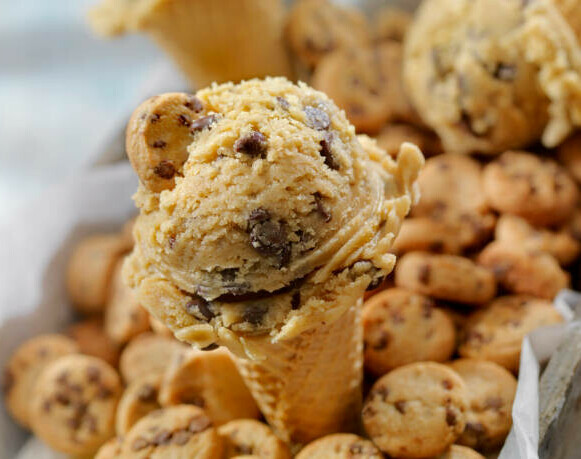 Easy Homemade Cookie Dough Ice Cream Recipe image 3 ice cream cone with scoops of cookie dough ice cream sat in pile of cookies frosted fusions