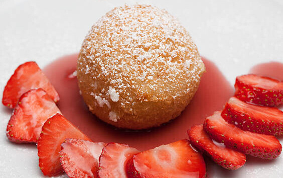 Hot Meets Cold Learn how to Make Deep Fried Ice Cream image 2 deep fried ice cream ball dusted with icing sugar on plate with freshly sliced strawberries and strawberry sauce frosted fusions