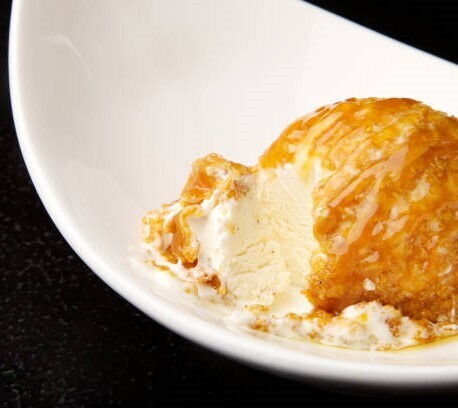 Hot Meets Cold Learn how to Make Deep Fried Ice Cream image 3 white dish with scoop of deep fried ice cream cut open with caramel sauce drizzled atop frosted fusions