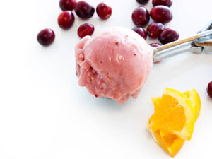 Homemade-Cranberry-Orange-Ice-Cream-Recipe-image-6-scoop-of-cranberry-and-orange-ice-cream-in-ice-cream-scoop-with-fresh-cranberries-and-slices-of-fresh-orange-frosted-fusions