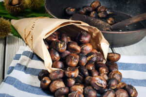 Homemade Roasted Chestnut Ice Cream Recipe image 2 roasted chestnuts served in a paper cone with pan in background with more roasted chestnuts frosted fusions
