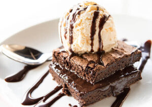 homemade-chocolate-brownie-ice-cream-recipe-image-2-plate-with-2-brownies-and-a-scoop-of-ice-cream-on-top-and-chocolate-sauce-drizzled-across-with-siler-spoon-frosted-fusions