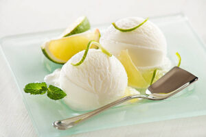 Dairy-Free-Coconut-Based-Frozen-Treats-–-Creamy-Dreamy-100-Delicious-image-1-glass-dish-with-coconut-scoops-of-ice-cream-garnished-with-slices-of-limes-with-a-silver-spoon-frosted-fusions