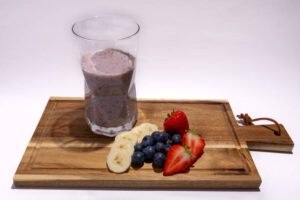 What-Smoothie-Is-Best-For-The-Immune-System-image-5-blueberries-strawberries-anbd-banana-sliced-on-wooden-chopping-board-with-glass-of-smoothie-Frosted-Fusions