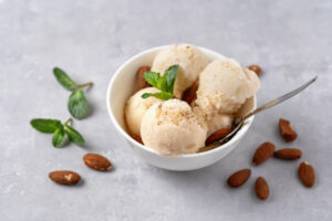 Homemade-Dairy-Free-Almond-Milk-Ice-Cream-Recipe-image-3-bowl-of-almond-milk-ice-cream-with-fresh-almonds-to-the-side-and-sprigs-of-green-leaves-Frosted-Fusions