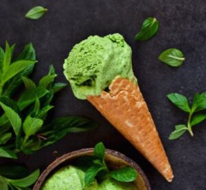 Homemade-Ice-Cream-Infused-With-Herbs-image-2-green-ice-cream-in-a-waffle-cone-with-a-selection-of-herbs-to-the-side-dark-background-Frosted-Fusions