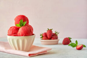 Homemade-Strawberry-Sorbet-Recipe-image-4-strawberry-sorbet-in-white-bowl-with-fresh-strawberries-scattered-to-the-side-Frosted-Fusions