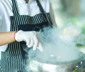 Celebrating Women Who Shaped Ice Cream For International Women’s Day image 6 person wearing apron stirring a large silver pot of liquid nitrogen ice cream Frosted Fusions