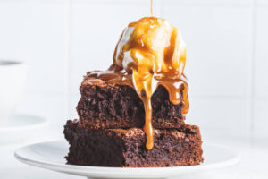 Classic Fudge Meets Chocolate Fudge Ice Cream – Trendy Nostalgia image 2 chocolate brownies with scoop of ice cream and caramel sauce drizzled on top Frosted Fusions