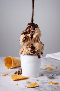 Classic-Fudge-Meets-Chocolate-Fudge-Ice-Cream-–-Trendy-Nostalgia-image-4-chocolate-fudge-ice-cream-with-waffle-cones-and-chocolate-sauce-being-drizzled-Frosted-Fusions