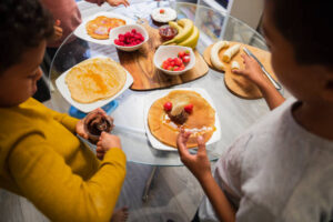 Holy-Crepe-Homemade-Pancake-Ice-Cream-image-2-table-laid-out-with-pancakes-and-topping-ingredients-with-kids-topping-pancakes-Frosted-Fusions