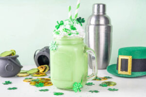 Mint-To-Be-Shamrock-Shake-Ice-Cream-Recipes-For-St.-Patricks-Day-image-7-shamrock-shake-in-glass-with-shamrocks-gold-coins-and-traditional-Irish-Green-hat-Frosted-Fusions