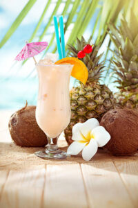 Pina-Colada-Sorbet-Ice-Cream-–-The-Best-Of-Both-Worlds-image-1-pina-colada-in-tall-glass-with-umbrellas-with-beach-setting-in-the-background-Frosted-Fusions