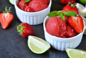Strawberry-Daiquiri-Sorbet-–-A-Boozy-Cocktail-Inspired-Frozen-Treat-image-5-strawberry-daiquiri-sorbet-in-white-dishes-with-fresh-limes-and-strawberries-Frosted-Fusions