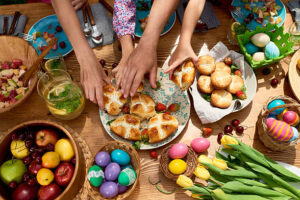Easy No-Churn Easter Ice Creams – Festive Fun For All Ages image 1 top view of hands reaching for Easter goodies incuding hot cross buns Frosted Fusions