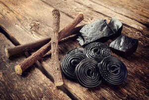 National Liquorice Day – Meets A Bold, Homemade Ice Cream image 5 piueces of liquorice in natural form and black rolls and stick form with wooden background Frosted Fusions
