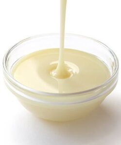 Troubleshooting-Tips-And-Tricks-For-No-Churn-Ice-Cream-image-2-glass-dish-of-sweetened-condensed-milk-being-drizzled-white-background-Frosted-Fusions