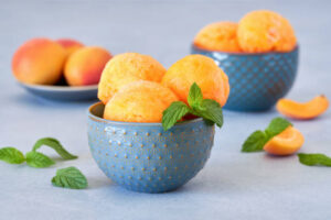 Naturally Sweet Sorbets For Summer – Healthy, Easy Dessert Ideas image 4 bowl of peach sorbet with fresh green leaves and slices of peach Frosted Fusions
