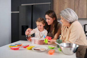 Fun-Easy-Homemade-Ice-Lollies-Popsicles-—-The-Perfect-Summer-Treat-image-2-two-women-helping-a-child-make-ice-lollies-with-fresh-fruit-to-the-side-Frosted-Fusions