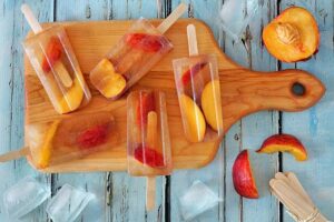 Homemade Peach Ice Cream And Lollipops Recipes Image 3 top view of ice lollies with peach pieces and fresh peach to the side Frosted Fusions
