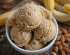 Vegan-Desserts-Exciting-Healthy-Unique-Plant-Based-Ice-Cream-Recipes-image-5-Peanut-and-banana-ice-cream-in-a-bowl-with-fresh-bananas-and-cashews-in-the-background-Frosted-Fusions